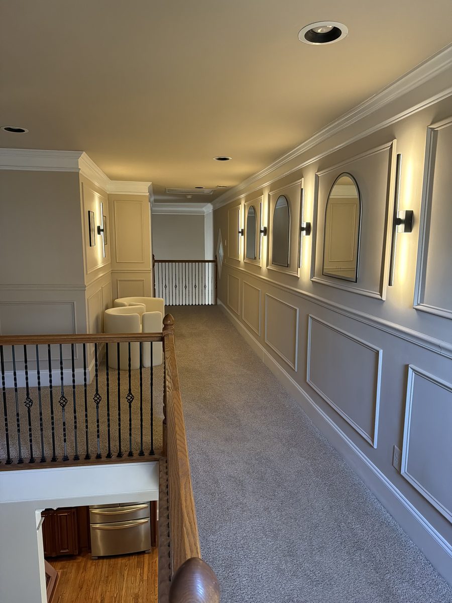 Finished hallway with two-tone panelled wainscot, arched mirrors and slim vertical sconces.