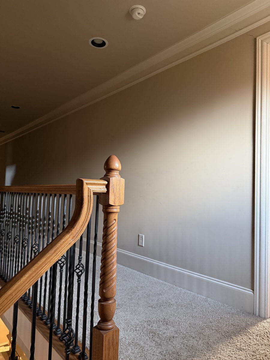Before: the upstairs landing wall in flat paint above carpet, with no detail beyond the baseboard and crown.